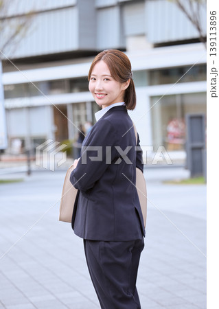 オフィス街を歩く笑顔の若い女性ビジネスパーソン・紺色スーツ姿で通勤する日本人会社員 オフィス街を歩く笑顔の若い女性ビジネスパーソン・紺色スーツ姿で通勤する日本人会社員 139113896