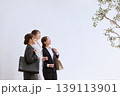 オフィスビルの前で上を見上げる笑顔の若手女性ビジネスパーソン3人・スーツ姿の新入社員・就職活動 139113901