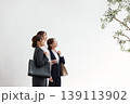 白い壁の前で上を見上げる三人のリクルートスーツ姿の若い女性・就職活動中の女子大学生 139113902