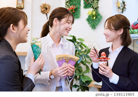 カフェでクレープやスイーツを手に楽しく会話する3人の若い女性ビジネスウーマン・仕事仲間とのスイーツタ 139113905