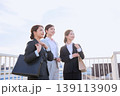 朝の通勤風景・笑顔で前を見つめるスーツ姿の若い女性ビジネスパーソン3人が橋の上に並ぶ 139113909