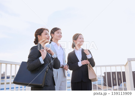 朝の通勤風景・笑顔で前を見つめるスーツ姿の若い女性ビジネスパーソン3人が橋の上に並ぶ 朝の通勤風景・笑顔で前を見つめるスーツ姿の若い女性ビジネスパーソン3人が橋の上に並ぶ 139113909