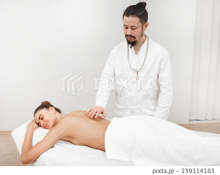 Doctor of traditional oriental medicine doing non contact energetic massage to a beautiful woman in a spa salon. The body is cleansed of negative energy. Reiki massage 139114183