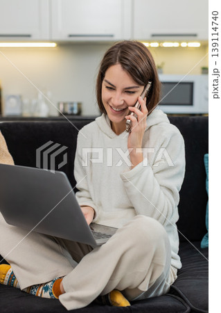 Young woman works on laptop and talks on smartphone multitasks with call focused typing in real time Young woman works on laptop and talks on smartphone multitasks with call focused typing in real time 139114740