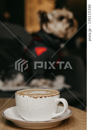 Close-up of latte art coffee with blurred cute dog in background. Pet-friendly cafe atmosphere, cozy morning lifestyle, urban dog owner routine, aesthetic ceramic cup, stylish pet-friendly interior. Close-up of latte art coffee with blurred cute dog in background. Pet-friendly cafe atmosphere, cozy morning lifestyle, urban dog owner routine, aesthetic ceramic cup, stylish pet-friendly interior. 139115390