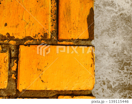 Close-up of old yellow brick wall with cracked texture and concrete corner. Grungy industrial background, urban architectural detail with aged paint. 139115446