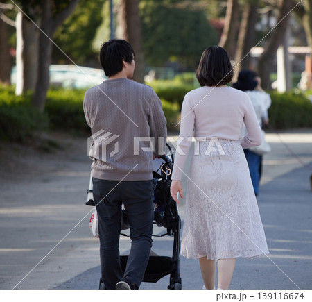 春の公園でベビーカーを持って散歩する若い夫婦の姿 春の公園でベビーカーを持って散歩する若い夫婦の姿 139116674