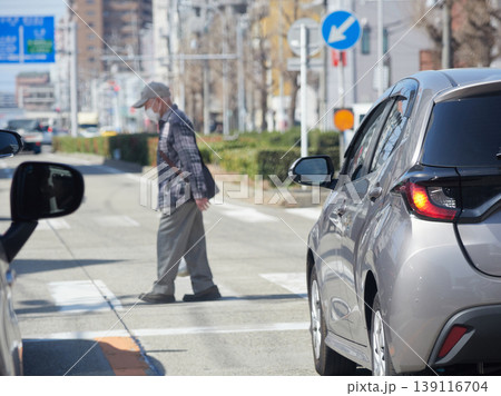 通勤途中の都市の道路上で信号待ちの車の様子と横断歩道を渡るシニア男性の姿 通勤途中の都市の道路上で信号待ちの車の様子と横断歩道を渡るシニア男性の姿 139116704