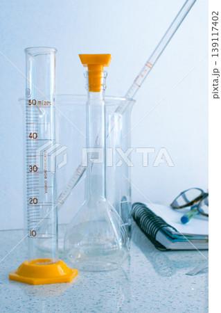 Laboratory glassware including a measuring cylinder, flask with stopper, and beaker are prepared on a counter, facilitating scientific research, chemical analysis, and medical advancements 139117402