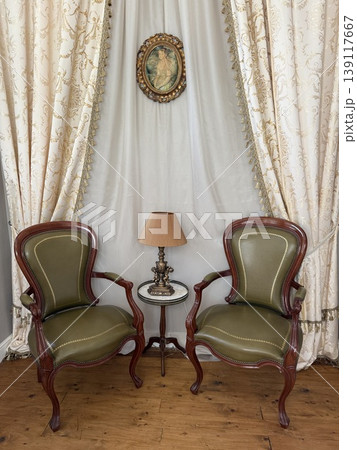 Victorian-style sitting area with ornate chairs and table against elegant draped curtains background 139117667