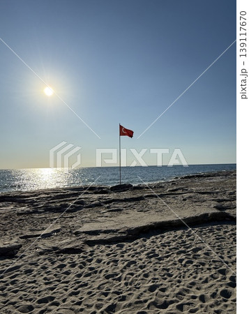 Beach scene with red warning flag and sun over ocean horizon, ideal for background or travel concept 139117670