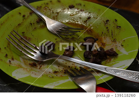 Messy leftover meat chunks and dark sauce residue on a lime green patterned plate with silver forks Messy leftover meat chunks and dark sauce residue on a lime green patterned plate with silver forks 139118260