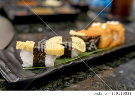 Assorted Japanese sushi platter featuring tamago nigiri with egg omelet and nori seaweed, followed by rolls with fish roe. Close-up shot on black plate in restaurant setting. Delicious Asian cuisine. Assorted Japanese sushi platter featuring tamago nigiri with egg omelet and nori seaweed, followed by rolls with fish roe. Close-up shot on black plate in restaurant setting. Delicious Asian cuisine. 139119031
