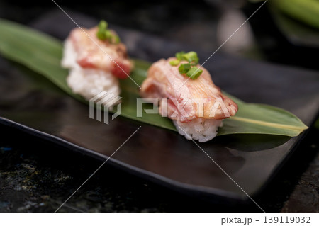 Two pieces of premium seared wagyu beef or tuna nigiri sushi garnished with green onions on a bamboo leaf and black ceramic plate. High-end Japanese gourmet cuisine with shallow depth of field. 139119032