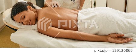 Asian woman enjoys acupuncture procedure lying on massage table at wellness spa 139120869