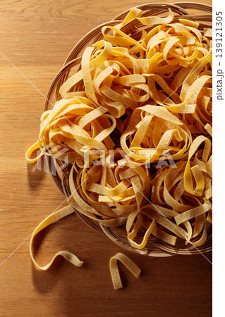 Raw dry pasta fettuccine in wicker dish on a wooden table. 139121305