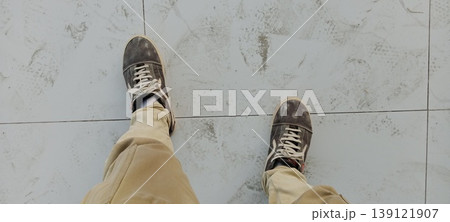 Top View of Person Wearing Dirty Sneakers and Beige Pants Standing on White Marble Tile Floor Top View of Person Wearing Dirty Sneakers and Beige Pants Standing on White Marble Tile Floor 139121907