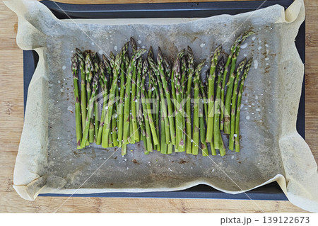 Overhead view of fresh green asparagus arranged on parchment paper lined baking sheet, raw and uncooked, rustic minimal food prep mood Overhead view of fresh green asparagus arranged on parchment paper lined baking sheet, raw and uncooked, rustic minimal food prep mood 139122673