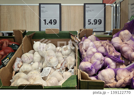 Supermarket produce section with white Chinese garlic and purple Italian garlic variety in mesh bags inside cardboard boxes, price labels 139122770