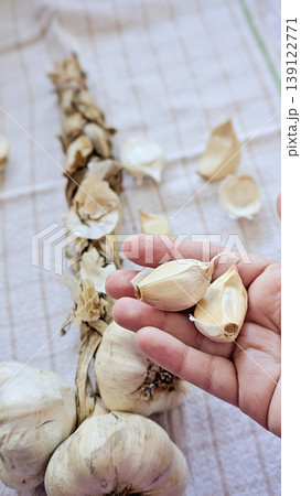 Vertical detail shot of dried garlic string braid with whole bulbs and loose cloves on green striped white linen cloth, warm natural tones Vertical detail shot of dried garlic string braid with whole bulbs and loose cloves on green striped white linen cloth, warm natural tones 139122771