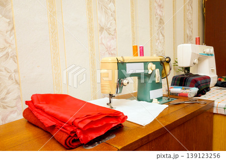 old green sewing machine on a wooden table with red fabric old green sewing machine on a wooden table with red fabric 139123256