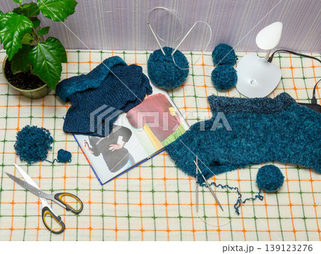 top view of a table with blue yarn knitting and an instruction book by a plant 139123276