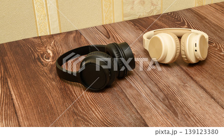 black and beige headphones lying on the edge of a wooden table in the room interior black and beige headphones lying on the edge of a wooden table in the room interior 139123380