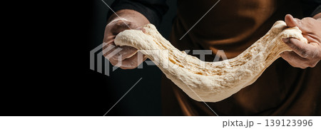 Baker stretching elastic dough showing gluten texture on dark background artisan baking concept Baker stretching elastic dough showing gluten texture on dark background artisan baking concept 139123996