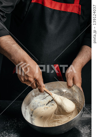 Baker mixing elastic dough in metal bowl with spoon homemade baking process Baker mixing elastic dough in metal bowl with spoon homemade baking process 139124037