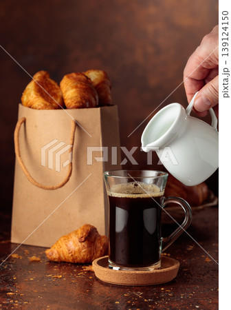Coffee latte and paper bag with croissants on a brown background. 139124150