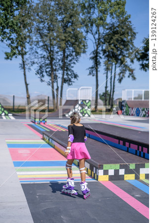 The girl confidently and professionally roller skates on the playground of the skate park. Rear view. 139124267
