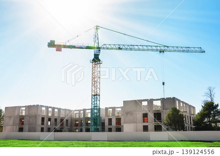 Large construction crane building a modern concrete block residential building under a bright blue sky with bright sunshine. Urban development and architecture concept. 139124556