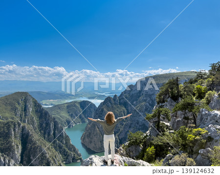Hiker woman on the background of a mountain river. Girl traveler stands on the edge of rock 139124632