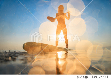 Silhouette of girl walking on sup board by the sea during summer vacation Silhouette of girl walking on sup board by the sea during summer vacation 139124641