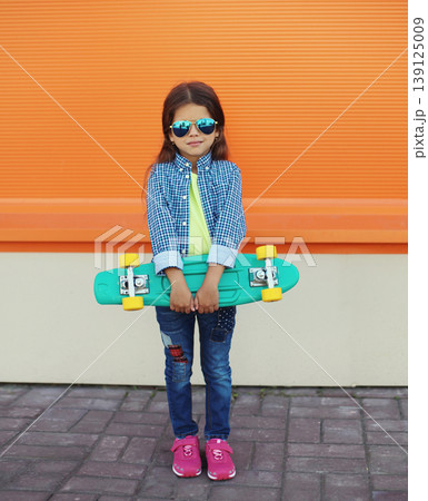 Stylish girl child with skateboard posing in the city Stylish girl child with skateboard posing in the city 139125009