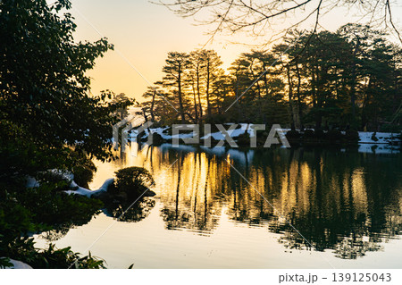 朝の兼六園 蓬莱島と朝日が映る霞ヶ池の水面 139125043