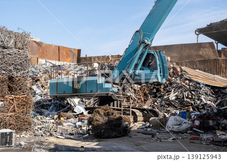 Excavator loading scrap metal onto truck in junkyard. Excavator loading scrap metal onto truck in junkyard. 139125943