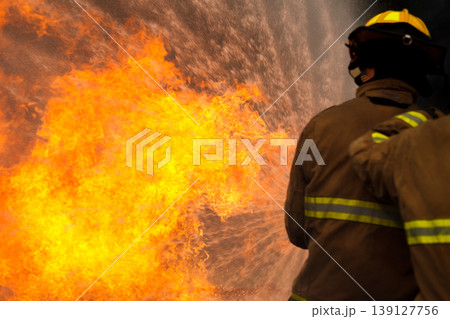 Professional fire fighters extinguishing intense fire with water hose 139127756