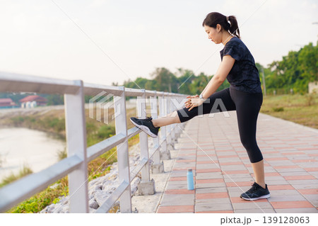 Asian woman in sportswear stretching her leg on park fence 139128063