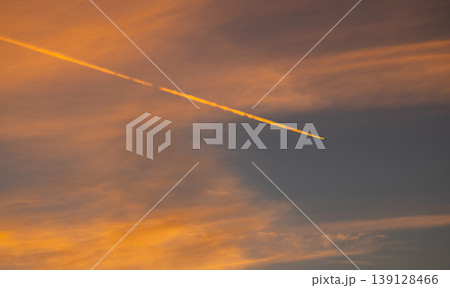Airplane contrail streaking across a dramatic orange sunset sky with soft clouds and warm golden light, minimalist atmospheric background 139128466