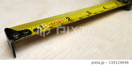 Close-up image of a measuring tape being rolled over a wooden surface. Close-up image of a measuring tape being rolled over a wooden surface. 139129046