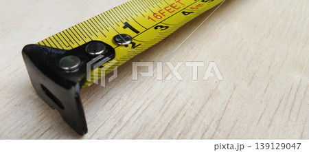 Close-up image of a measuring tape being rolled over a wooden surface. Close-up image of a measuring tape being rolled over a wooden surface. 139129047