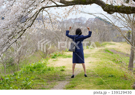 桜の下でガッツポーズをするスーツ姿の女性の後ろ姿 139129430