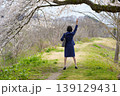 桜の下で手を挙げるスーツ姿の女性の後ろ姿 139129431