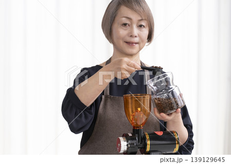リビングでコーヒー豆を挽いてコーヒーを飲むシニア女性 リビングでコーヒー豆を挽いてコーヒーを飲むシニア女性 139129645