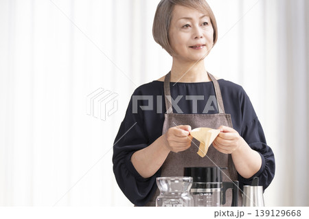 リビングでコーヒー豆を挽いてコーヒーを飲むシニア女性 139129668
