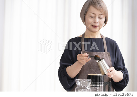 リビングでコーヒー豆を挽いてコーヒーを飲むシニア女性 139129673