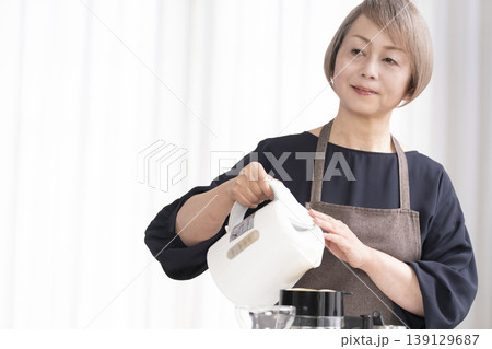 リビングでコーヒー豆を挽いてコーヒーを飲むシニア女性 リビングでコーヒー豆を挽いてコーヒーを飲むシニア女性 139129687