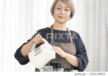 リビングでコーヒー豆を挽いてコーヒーを飲むシニア女性 リビングでコーヒー豆を挽いてコーヒーを飲むシニア女性 139129693