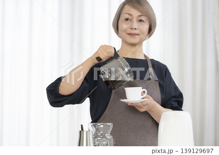 リビングでコーヒー豆を挽いてコーヒーを飲むシニア女性 リビングでコーヒー豆を挽いてコーヒーを飲むシニア女性 139129697
